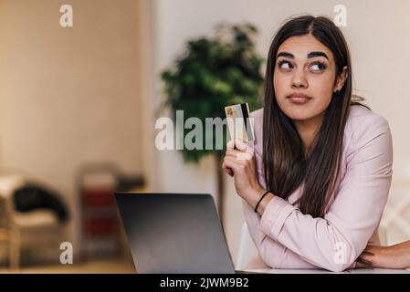 Seriöse junge Brünette Erwachsene Frau, denken darüber nach, wie viel Geld sie auf ihrer Debitkarte hat. Stockfoto