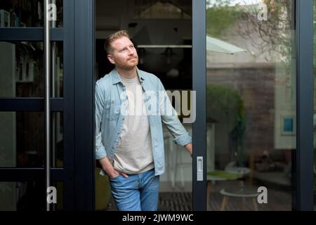 Grinsender junger, erwachsener bärtiger Mann, der draußen das Wetter überprüft und frische Luft bekommt. Stockfoto