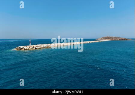 Meereslandschaft mit kleinem Leuchtturm auf Wellenbrecher, der zur Insel Palatia mit dem Tempel von Apollo Portara auf Naxos führt Stockfoto