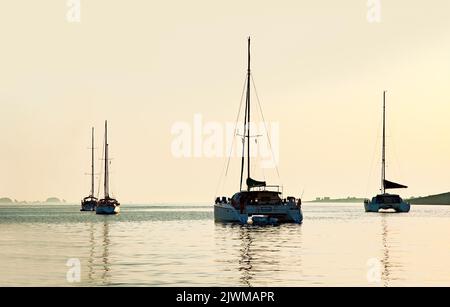 Ein paar Yachten bei Sonnenuntergang an der Paros Road Stead in Griechenland Stockfoto