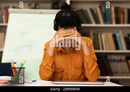 Müde junge schwarze Dame Gefühl Stress, verärgert über Fristen und Probleme, leiden unter Kopfschmerzen, sitzen in der Bibliothek Stockfoto