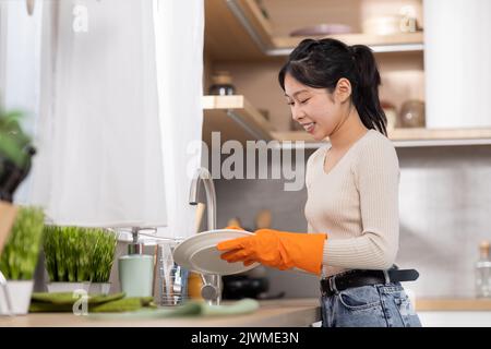 Fröhliche chinesische Frau, die zu Hause Geschirr wäscht Stockfoto