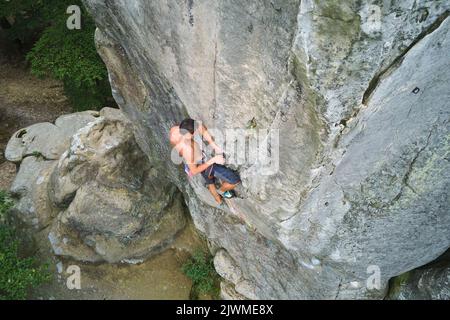 Entschlossener Kletterer, der die steile Wand des felsigen Berges hochklettert. Sportler überwinden schwierige Route. Extremsport und Klettern Stockfoto