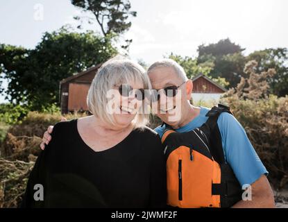 Rentnerpaar lachend am Strand bereit, Wassersport zu treiben Stockfoto