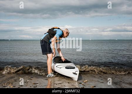 Pensionierter Mann auf dem Weg ins Meer, um in einem Kajak zu trainieren Stockfoto