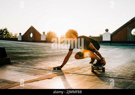 Porträt eines Mannes, der bei Sonnenuntergang auf einem Parkplatz Skateboarding Stockfoto