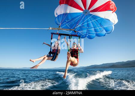 Zwei Frauen lächeln, während sie einen klaren Sommermorgen des Parasailings genießen. Stockfoto