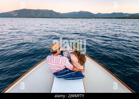 Ein Paar sitzt auf dem Bug einer Yacht, während sie während des Sonnenuntergangs kreuzen. Stockfoto