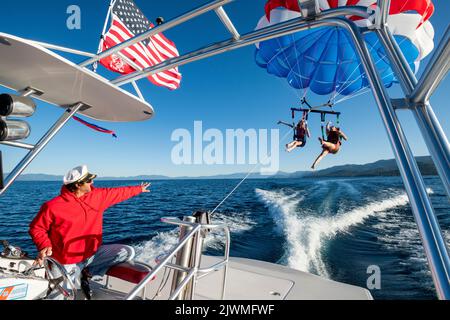 Der Kapitän winkt, als er zwei Frauen zum Parasailing schickt. Stockfoto