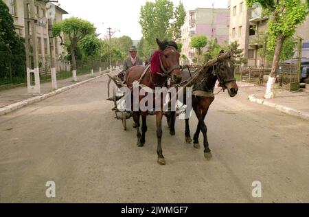 Ein Bauer reitet 1990, wenige Monate nach dem Fall des Kommunismus, mit seinem Pferdewagen durch eine Stadt in Rumänien. Viele Dörfer wurden während der kommunistischen Periode in städtischen Regionen gewaltsam umgewandelt, in denen eine Fabrik und Wohngebäude sowjetischer Art errichtet wurden. Die Einheimischen setzten ihre traditionelle Lebensweise so weit wie möglich fort. Ein Pferd und ein Karren waren selten, da diese normalerweise von der Regierung genommen wurden, um „gemeinsam“ verwendet zu werden. Stockfoto