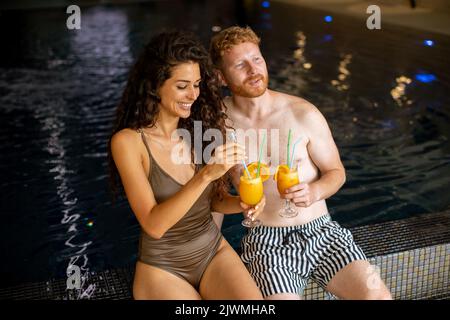 Schönes junges Paar, das sich entspannt und frischen Orangensaft am Pool trinkt Stockfoto