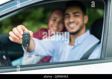 Probefahrt Transport. Frohes glückliches tausendjähriges arabisches Weib in Hijab und Mann zeigen Schlüssel von neuem Auto Stockfoto