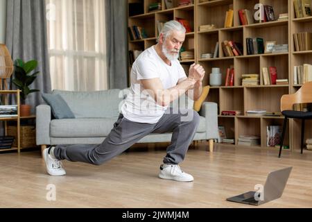 Grauhaariger reifer Mann, der zu Hause trainiert und ein Fitnessvideo ansieht Stockfoto