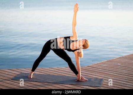 Sportliche Frau Mittleren Alters Praktiziert Yoga Im Freien, Stehend In Dreieckshaltung Stockfoto