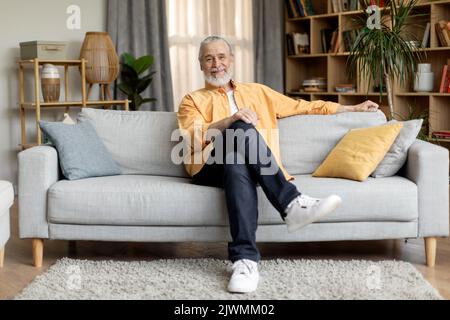 Entspannter älterer Mann, der zu Hause auf der Couch sitzt Stockfoto