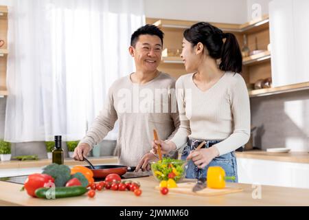Gesunde asiatische Familie von Vegetariern, die köstliche Mahlzeiten zubereiten Stockfoto