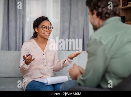Glückliche junge afroamerikanische Frau Arzt in Brille im Gespräch mit Patienten bei der Sitzung Stockfoto