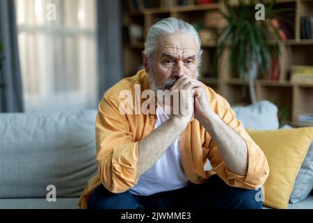 Nachdenklicher älterer Mann, der allein auf der Couch sitzt, häusliche Innenausstattung Stockfoto