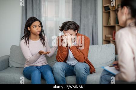 Traurige schwarze Frau beruhigt depressiven europäischen Ehemann auf Rücksprache mit Psychologe, Paar brauchen professionelle Hilfe Stockfoto