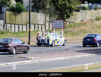 Ein vorbeifahrendes Polizeiauto kümmert sich um die beiden jungen Touristen, die auf einer verkehrsreichen Hauptstraße in Taupo nahe dem Zentrum Neuseelands unterwegs waren Stockfoto