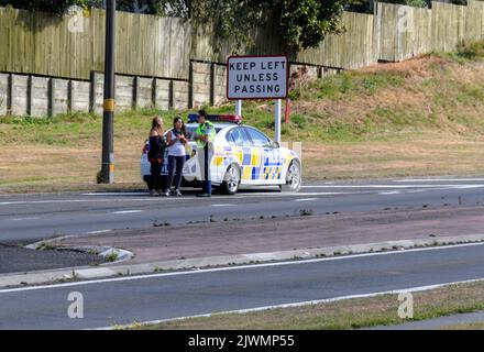 Ein vorbeifahrendes Polizeiauto kümmert sich um die beiden jungen Touristen, die auf einer verkehrsreichen Hauptstraße in Taupo nahe dem Zentrum Neuseelans zum Trampen unterwegs waren Stockfoto