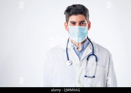 Porträt eines männlichen Arztes. Gesundheitsfachkraft trägt eine schützende Gesichtsmaske und steht auf einem isolierten weißen Hintergrund. Stockfoto