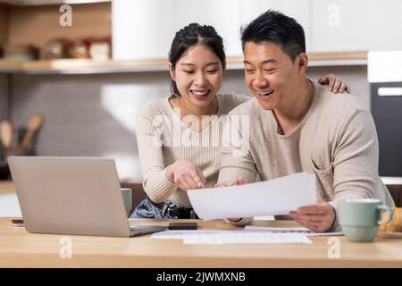 Fröhliche asiatische Ehegatten zahlen Rechnungen über das Internet, mit Laptop Stockfoto