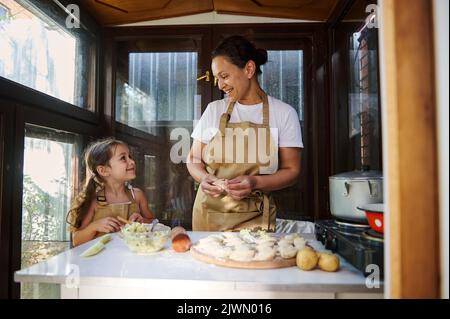 Charmante Frau hands-on varenyky, handgemachte Knödel, genießt das Kochen mit ihrem süßen kleinen Helfer, eine entzückende Tochter Stockfoto