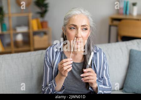 Konzentrierte kaukasische alte grauhaarige Dame, die Covid-19-Test alleine im Wohnzimmer macht Stockfoto