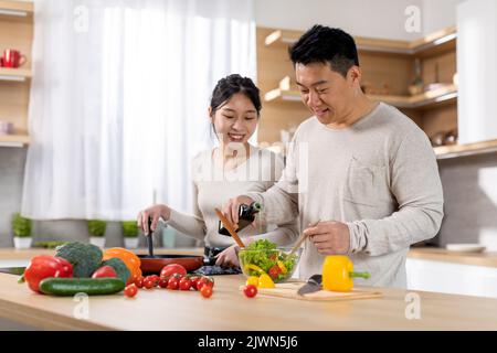 Fröhlicher koreanischer Ehemann und Ehefrau, die Gemüsesalat zubereitet Stockfoto