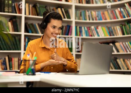 Ich mag Fernunterricht. Glückliche gemischte Rasse weibliche Lehrerin gestikuling Daumen nach oben, mit Online-Unterricht über Laptop Stockfoto