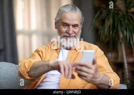 Einsamer älterer Mann, der auf der Couch sitzt und mit dem Handy telefoniert Stockfoto