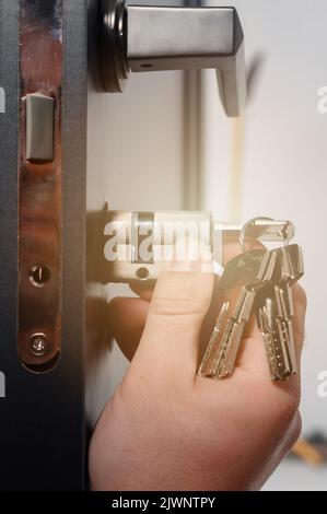 Der Master installiert den Kern für das Türschloss, Montagearbeiten mit der Tür, den Kern mit den Schlüsseln. Stockfoto