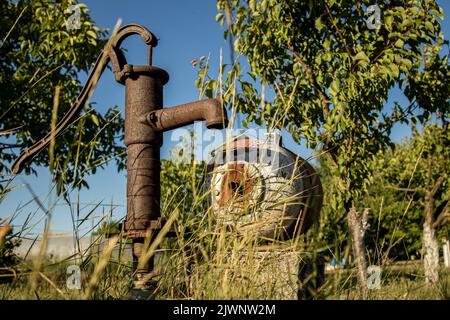 Traditionelle alte rostige Wasserpumpe, antiker Wasserbrunnen im Hinterhof Stockfoto