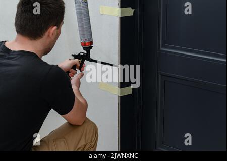 Die Verwendung von Befestigungsschaum mit einer Spritzpistole bei Bauarbeiten, Installation von Innentüren, Reparaturen im Haus. Stockfoto