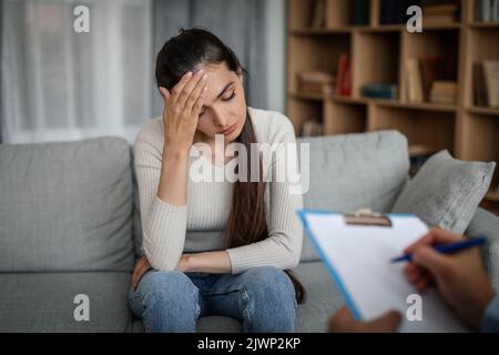 Verzweifelte junge kaukasische Frau, die an Depressionen leidet, hört sich im Büro einen männlichen Arzt an Stockfoto