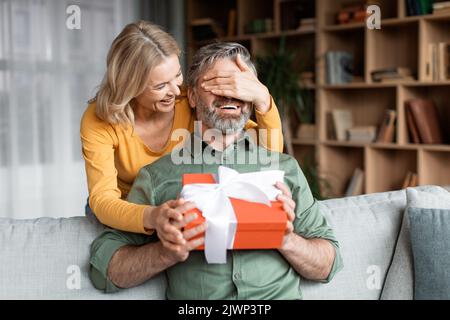 Liebevolle Frau Überraschende Mann Im Mittleren Alter Mit Geschenk Zu Hause Stockfoto