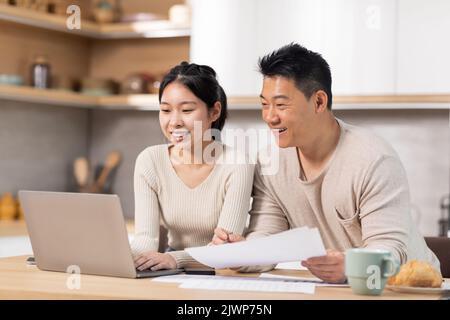 Fröhliches asiatisches Paar, das mit einem Laptop im Internet Rechnungen bezahlt Stockfoto