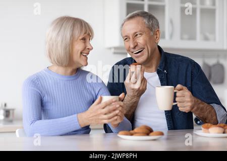 Glückliche ältere Ehepartner trinken zu Hause Tee mit Gebäck Stockfoto