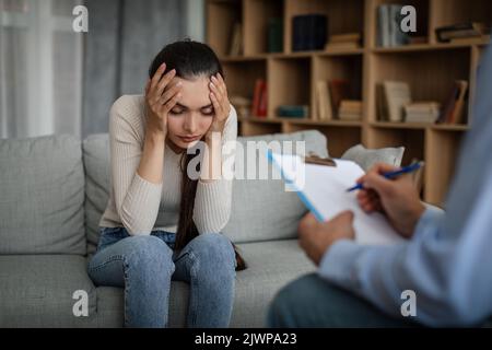 Verzweifelte, traurige junge kaukasische Dame, die an psychischen Problemen leidet, hört dem männlichen Arzt im Büro zu Stockfoto