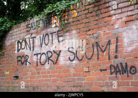 Graffiti-Worte auf einer britischen Ziegelwand im Freien: „Rettet den NHS und wählt nicht für Tory-Abschaum!“ Antikonservative, politische Meinung. Politik in Großbritannien. Stockfoto