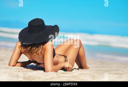 Alles, was Sie brauchen, ist Vitamin Meer. Rückansicht einer jungen Frau, die am Strand liegt. Stockfoto