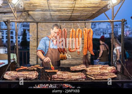 Frigiliana, Malaga, Spanien, 27. August 2022: Mann kocht Würstchen, Blutwurst und Rippchen auf dem Grill auf einem Grill Stockfoto