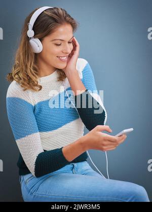 Gute Gefühle kommen von guten Liedern. Studioaufnahme einer jungen Frau, die vor grauem Hintergrund Musik hört. Stockfoto