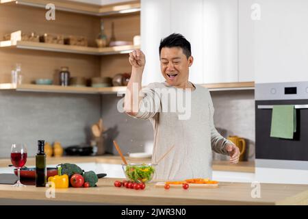 Lustige asiatische Mann salzen Essen, Küche Interieur Stockfoto