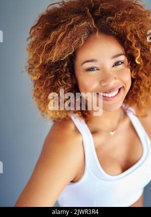 Glücklich zu sein geht nie aus der Mode. Eine sportliche junge Frau posiert vor grauem Hintergrund. Stockfoto