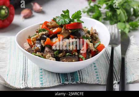 Warmer Salat mit Zunge, Aubergine und Paprika auf weißem Teller auf grauem Hintergrund Stockfoto