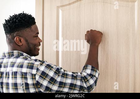Seitenansicht Des Afrikanischen Guy, Der Neben Geschlossener Tür Klopft Stockfoto