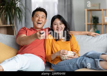 Entspannte chinesische Familie, die zu Hause gemeinsam Fernsehen schaut Stockfoto