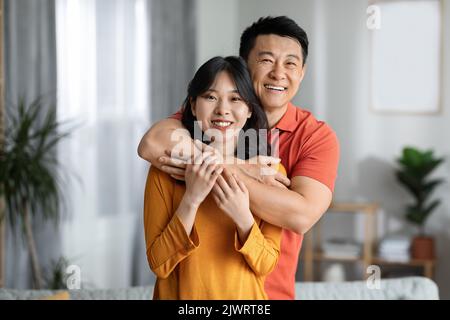Glückliche asiatische Mann und Frau umarmen zu Hause Stockfoto